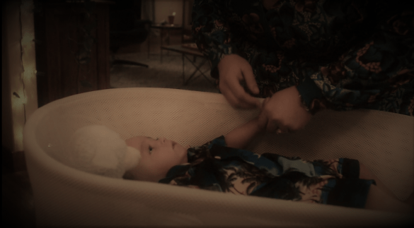 A screenshot from the show This is Us. A photo showing the character of Baby Jack in his bassinet, with his mother, Kate's hands reaching in towards him to lift him up.
